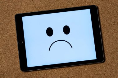 Açık mavi renk ve mantar arkaplan üzerine depresyon konseptini temsil eden hüzünlü bir yüzle bir tablete yaklaş