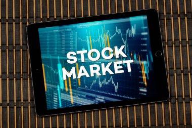 Grafik ve çizelge konsepti ve ahşap arkaplan üzerinde borsa tabiri olan bir tablete yakın durun.
