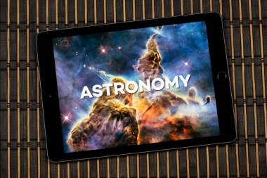 Bulanık bir nebula ya da galaksi üzerinde astronomi ifadesi olan dijital tablete yakın ve ahşap bir arkaplan.