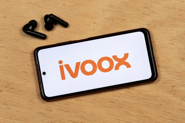 Akıllı telefon ekranının makro fotoğrafı ahşap arka planda kablosuz kulaklıkla portakal uygulamalı logoyu gösteriyor.