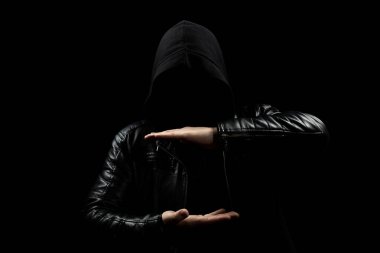 Yüzü olmayan kapüşonlu bir adama yakın. İki eli önünde ve siyah bir geçmişi olan özel bir yer gösteriyor.