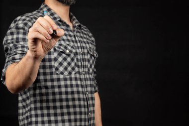 Önündeki boşlukta sağ eli ve siyah bir arkaplan ile yazan genç bir adama yakın durun.