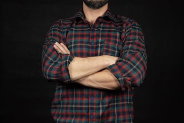 Oduncu gömleği giyen, kollarını kavuşturmuş, önünde el kol hareketi yapan ve siyah arka planı olan bir adama yaklaş.