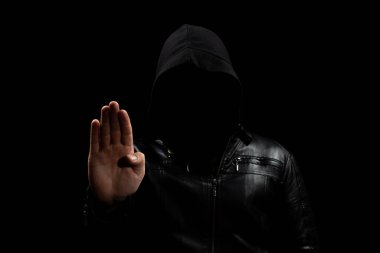 Gölgelerde yüzsüz, kapüşonlu bir hacker 'a yaklaş. Sağ eli dur işareti yapıyor ve siyah bir arka plan oluşturuyor.