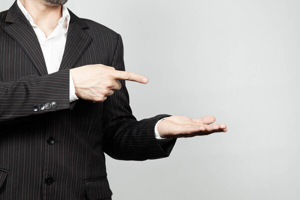 Близко к бизнесмену в костюме, пытающемуся показать что-то левой ладонью и указывающему правым указательным пальцем