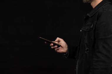 Ekranın sağ tarafında siyah kot ceket giyen, akıllı telefonlu ve siyah arka planlı mesajlaşan bir adama yaklaş.