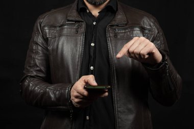 İşaret parmağıyla akıllı telefon ekranını gösteren kahverengi deri ceketli bir adama yaklaş.