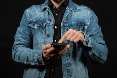 Kot ceket giyen, sağ elini cep telefonuna ve siyah arkaplana doğrultmuş bir adama yakın durun.