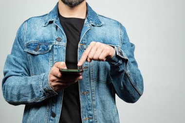 Ekranın sol tarafında kot ceket giyen bir adama yaklaş. İşaret parmağıyla akıllı telefon ekranını ve beyaz arka planı işaret ediyor.