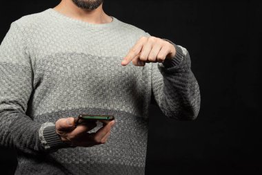 İşaret parmağıyla akıllı telefon ekranının üzerindeki boşluğu gösteren beyaz kazak giyen bir adama yaklaş.