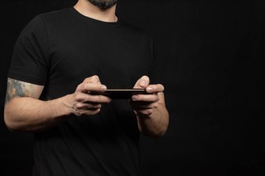 Ekranın sol tarafında siyah tişörtlü bir adama yaklaş. İki eliyle akıllı telefon tut.