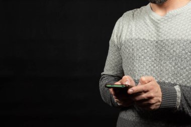 Ekranın sağ tarafında beyaz kazak giyen, elinde telefon ve siyah arka plan olan bir adama yaklaş.