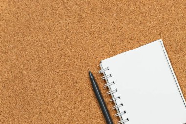 Ekranın sağ tarafında beyaz bir defter ve siyah bir kalemin mantar arkaplan üzerindeki makro fotoğrafı