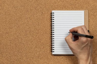 Ekranın sağ tarafındaki beyaz bir deftere mantar arkaplan üzerine yazı yazan bir erkeğe yaklaş