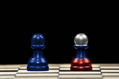 Satranç tahtası ve jeopolitik konseptte siyah arkaplan üzerinde Avrupa Birliği ve Rusya bayrakları olan iki piyona yakın satranç taşı