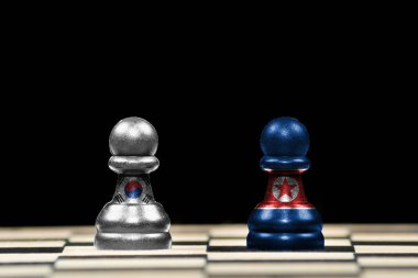 Bir satranç tahtası ve jeopolitik konseptte siyah bir zemin üzerinde Güney Kore ve Kuzey Kore bayraklı iki piyon taşı yakın