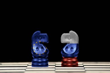 Satranç tahtası ve jeopolitik konseptte siyah arkaplan üzerinde Avrupa Birliği ve Rusya bayrakları olan iki ata yakın satranç taşı