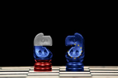 Satranç tahtası ve jeopolitik konseptte siyah arkaplan üzerinde Rusya ve Avrupa Birliği bayrakları olan iki ata yakın satranç taşı