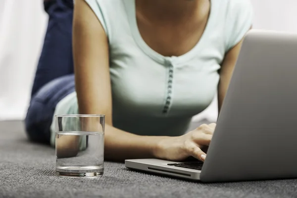 Mujer joven que pone mientras usa el ordenador portátil —  Fotos de Stock