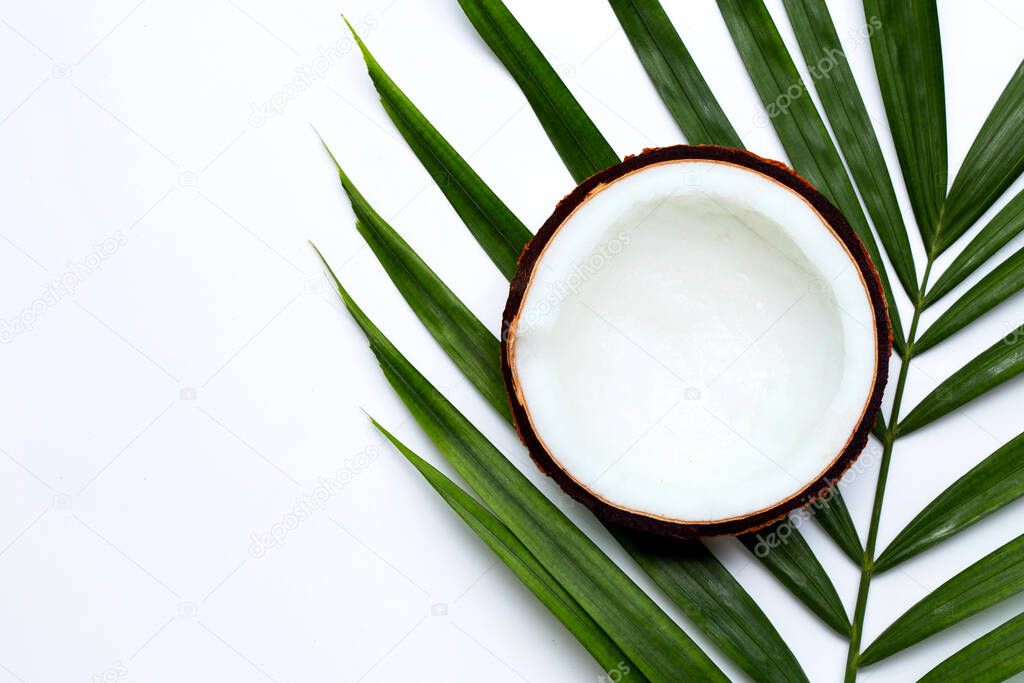 Half coconut on tropical palm leaves on white background. Top view