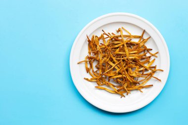 Kurutulmuş Lily Buds mavi arka planda beyaz tabakta. Boşluğu kopyala