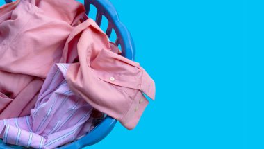 Mavi arka planda çamaşır sepetinde giysiler. Boşluğu kopyala