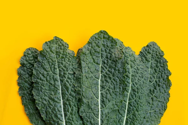 Fresh organic green kale leaves on yellow background.