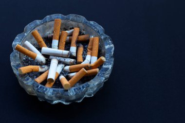 Sigara tomurcukları koyu arkaplanda şeffaf bir kül tablasında..