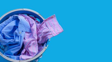 Mavi arka planda çamaşır sepetinde giysiler. Boşluğu kopyala