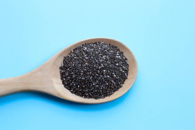 Mavi arka planda tahta kaşıkta Chia tohumları.