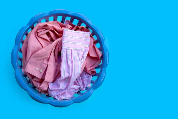 Clothes in a laundry basket on blue background. Copy space