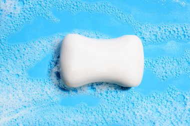 Mavi arkaplanda köpüklü sabun çubuğu.