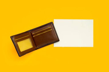 Sarı arka planda beyaz kağıtlı kahverengi cüzdan.