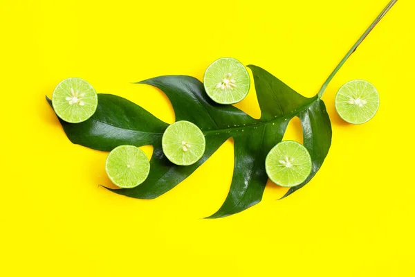 Fresh limes with green leaf on yellow background.