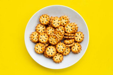 Sarı zemin üzerinde beyaz tabakta ananas bisküvileri.
