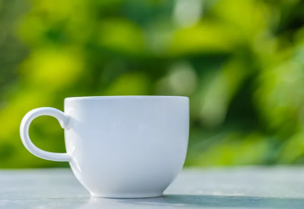 Cup of coffee on  table in green garden — Stock Photo, Image