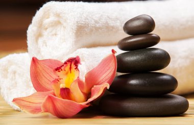 Spa arka planı. Egzotik bitkiler üzerinde beyaz havlular, güzel orkide çiçekleri ve rahatlatıcı spa masajı ve vücut bakımı için dengeleyici taşlar. Aromalı Asya ilaçları ve sağlıklı vücut için taş terapisi.