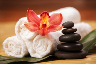 Spa arka planı. Egzotik bitkiler üzerinde beyaz havlular, güzel orkide çiçekleri ve rahatlatıcı spa masajı ve vücut bakımı için dengeleyici taşlar. Aromalı Asya ilaçları ve sağlıklı vücut için taş terapisi.