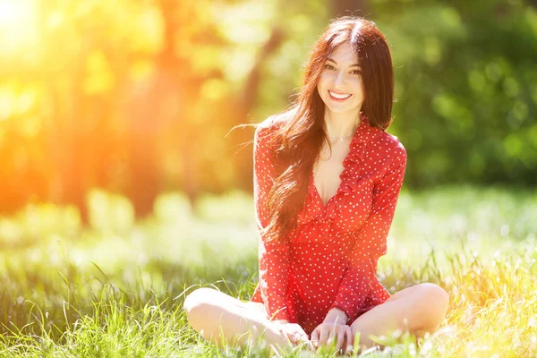 年轻可爱的女人穿着红色衣服在公园里放松 美丽的自然景观 背景五彩斑斓 树木盛夏时节 户外生活方式 快乐的微笑的女人坐在绿草上 — 图库照片