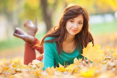 Genç ve güzel bir kadın sonbahar parkında dinleniyor. Renkli yeşillik arka planlı güzel doğa sahnesi, sonbahar mevsiminde sarı ağaçlar ve yapraklar. Sonbahar açık hava yaşam tarzı