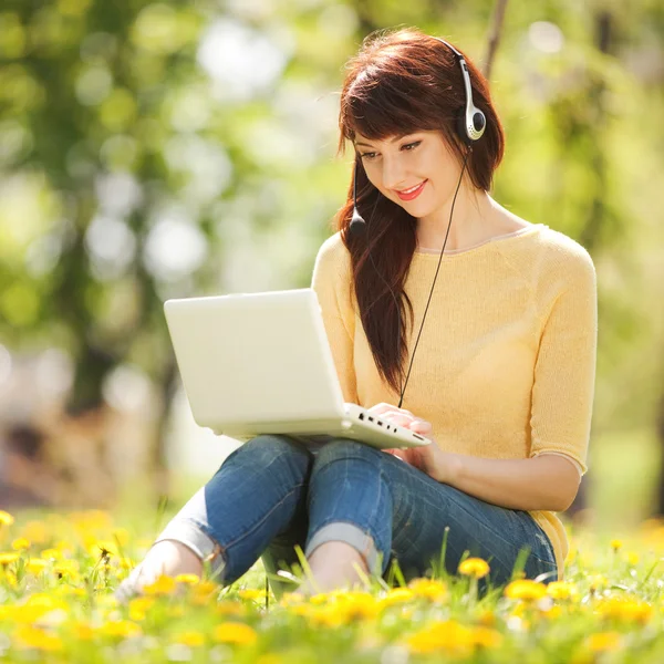 Mujer linda en auriculares con portátil blanco en el parque — Foto de Stock