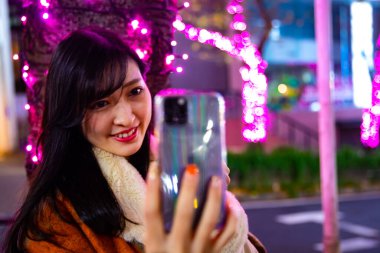 Japon bir kız, Shibuya 'nın aydınlık caddesinde gece selfie çekiyor.