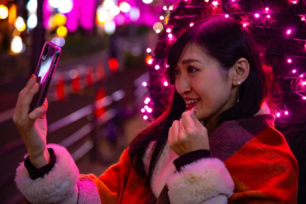 Japon bir kız, Shibuya 'nın aydınlık caddesinde gece selfie çekiyor.