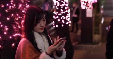 Japon bir kız Shibuya 'nın aydınlık caddesinde gece telefon ediyor.