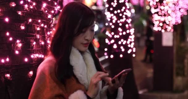 Uma menina japonesa chamando telefone à noite iluminado rua em Shibuya handheld — Vídeo de Stock