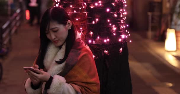 Una chica japonesa enviando un mensaje en la calle iluminada de noche en Shibuya de cerca — Vídeo de stock