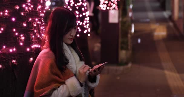 Una chica japonesa enviando un mensaje en la calle iluminada de noche en Shibuya de cerca — Vídeo de stock
