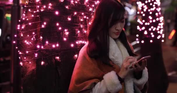 Japońska dziewczyna wysyła wiadomość w nocy oświetlona ulica w Shibuya bliski strzał handheld — Wideo stockowe