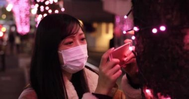 Maskeli bir Japon kız Shibuya 'daki gece sokağında ateş ediyor.