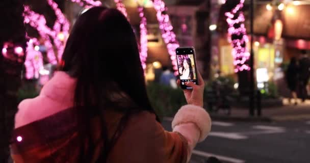 Uma menina japonesa tiro selfie à noite iluminado rua em Shibuya tiro de perto handheld — Vídeo de Stock